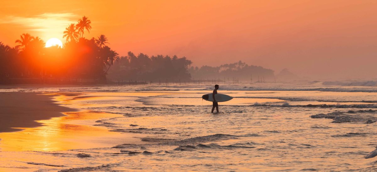 Silhouette of a surfer walking to the ocean during sunset. Active holiday at sea